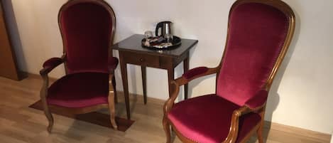 Two wooden chairs with red velvet upholstery and gold trim, positioned on a wooden floor with a patterned border.