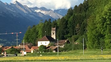 Un village rural avec une église dotée d’un clocher, entouré de montagnes et de verdure.