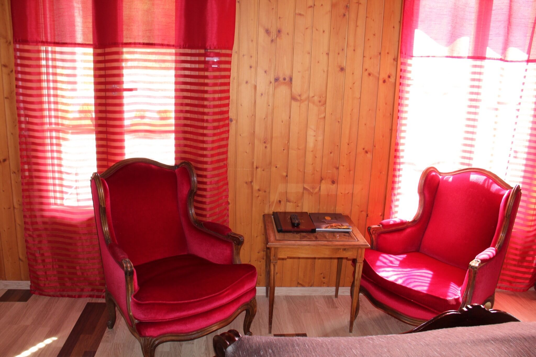 Une pièce avec deux fauteuils à accoudoirs en velours rouge et une petite table en bois sur laquelle se trouvent un livre et une télécommande.