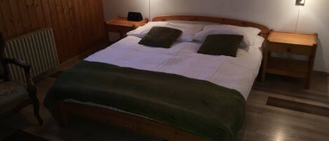 Una cama con estructura de madera, un edredón verde, dos mesitas de noche y lámparas fijadas a la pared.