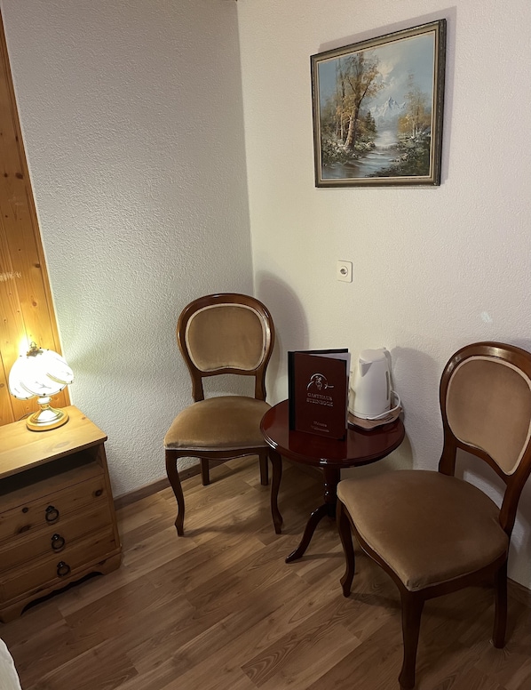 A room with two wooden chairs, a small round table, a lamp, and a framed painting on the wall. - Historic Hotel Steinbock (Gsteigwiler)