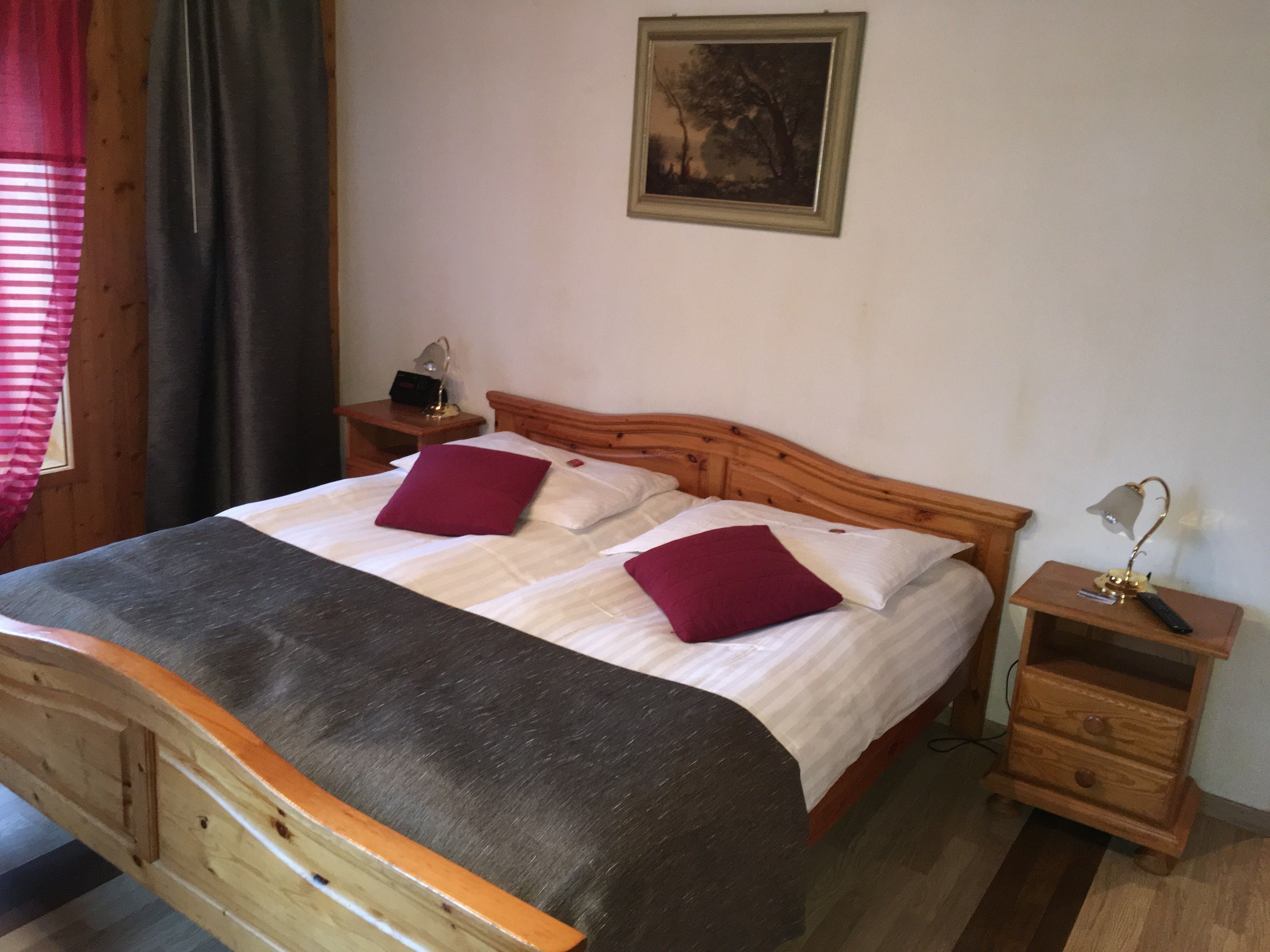 A neatly made bed with a wooden headboard, two pillows, a bedside table with a lamp, and a small drawer unit.