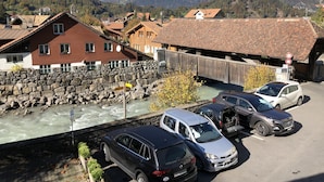 A parking area with cars, a stone wall, and a wooden bridge over a river. - Historic Hotel Steinbock (Gsteigwiler)
