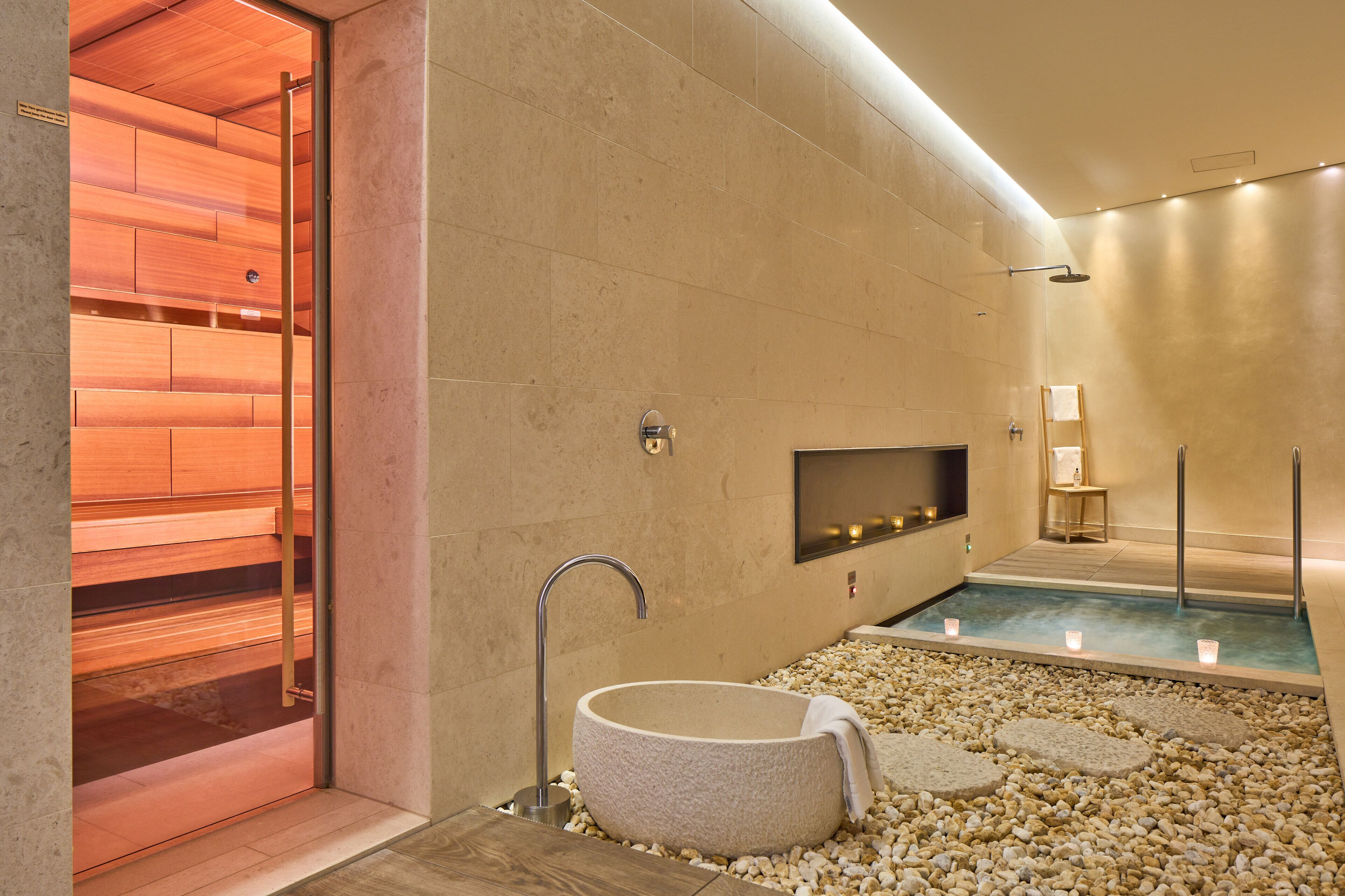 A modern bathroom with a freestanding bathtub, a wooden sauna, and a small seating area.