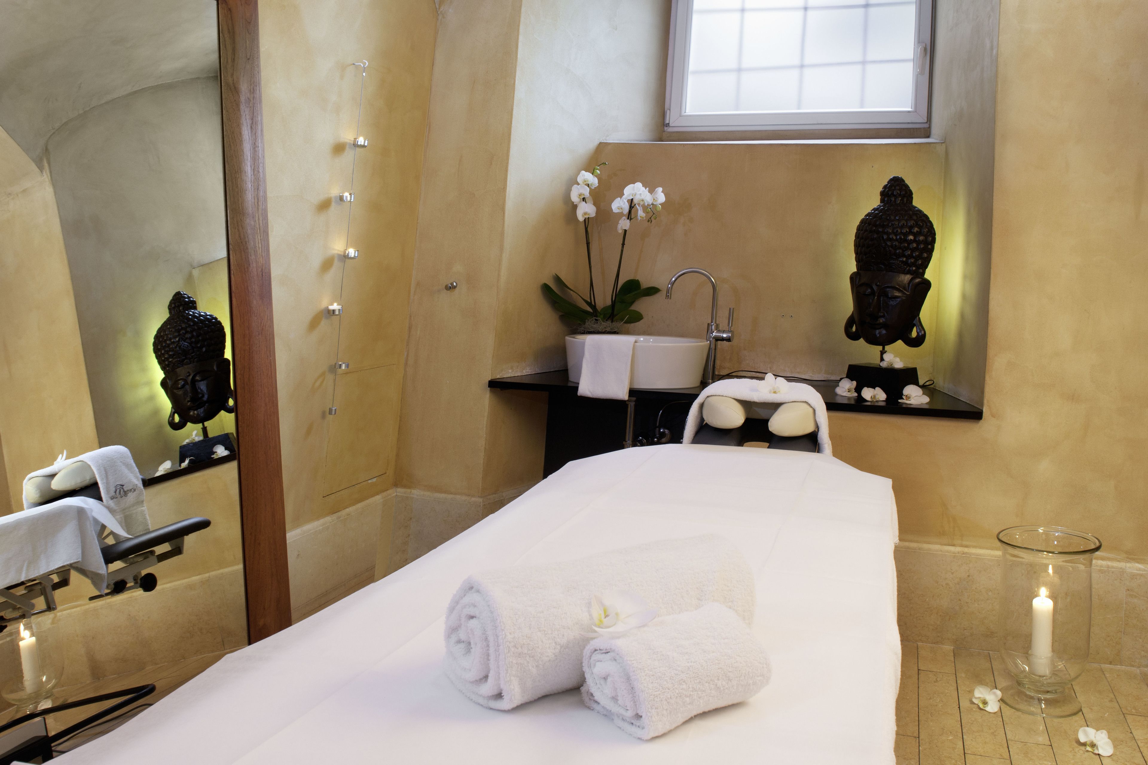 Een spa-ruimte met een massagetafel, handdoeken, een wastafel en decoratieve elementen.