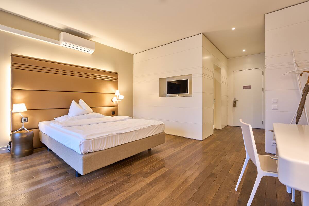 Une chambre d’hôtel moderne dotée d’un grand lit, de lampes de chevet, d’un téléviseur à écran plat et d’un coin repas avec une table et une chaise blanches.