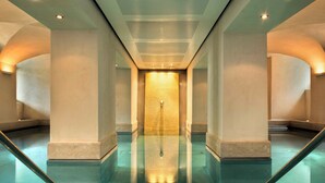 A modern indoor pool with clear glass walls, a central water feature, and a symmetrical architectural design.