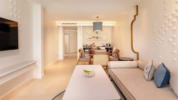 A modern living room with a flat-screen TV, a dining area with a chandelier, and a kitchen in the background.