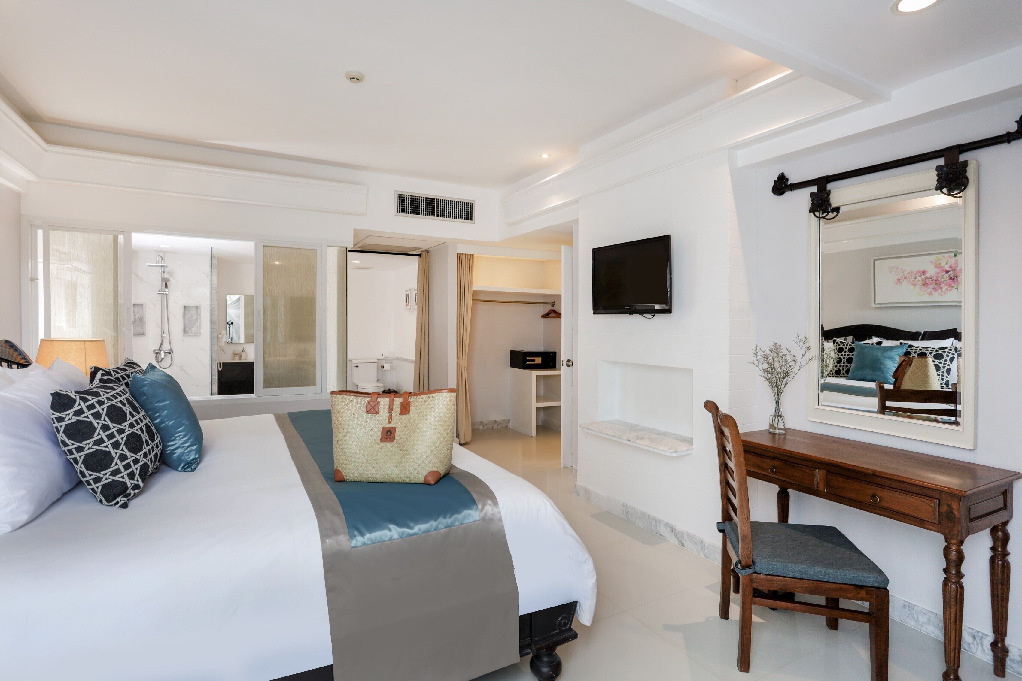 A hotel room with a large bed, a wooden desk, a chair, a TV, and a mirror.