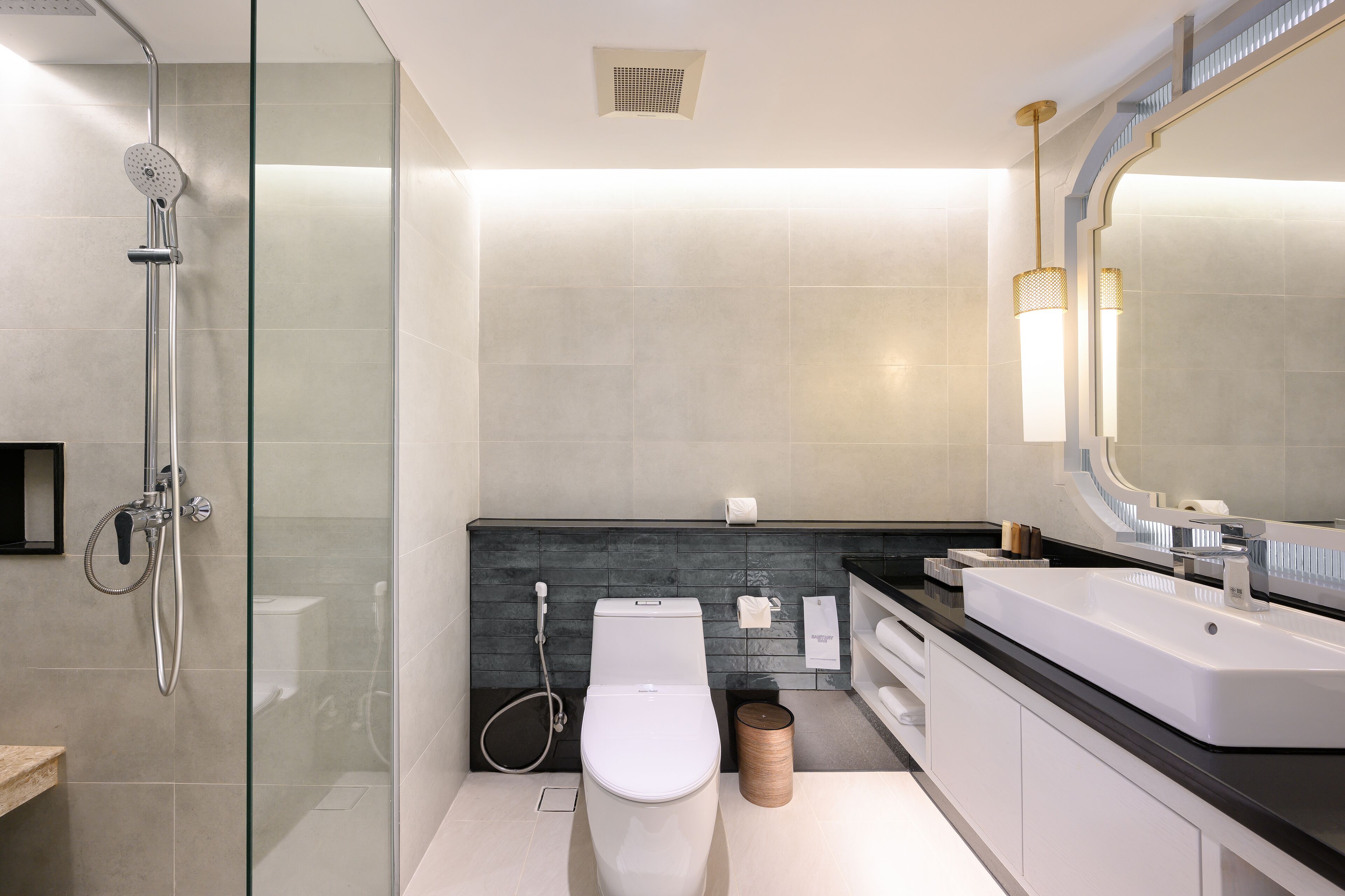 Un baño moderno con ducha envuelta en vidrio, inodoro blanco y un espejo grande sobre un mostrador negro.