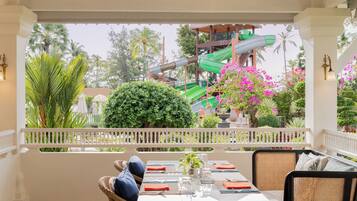 A dining area with a table set for two, overlooking a water park with slides and lush greenery.