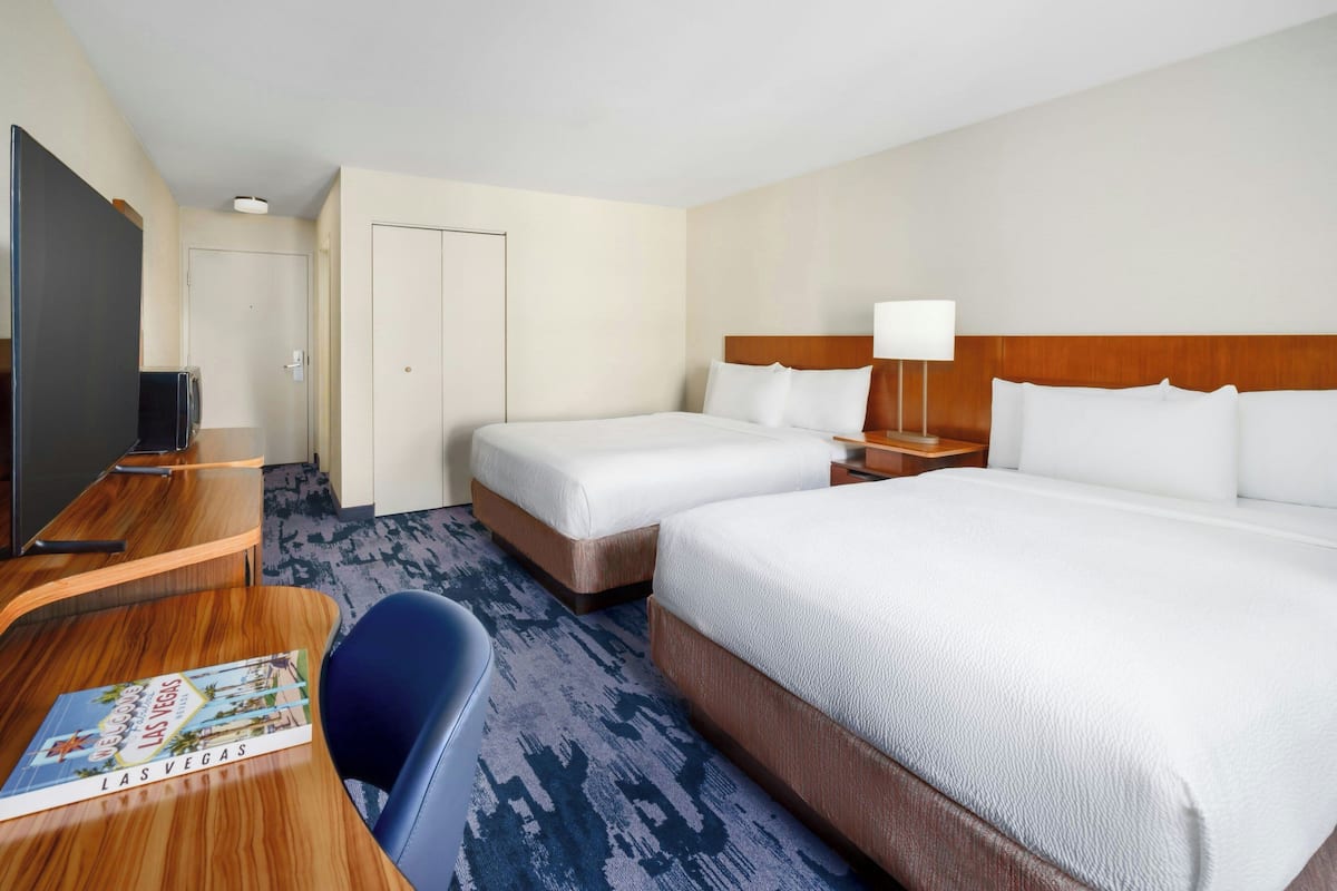 A hotel room with two beds, a desk with a computer, a TV, and a brochure on the desk.