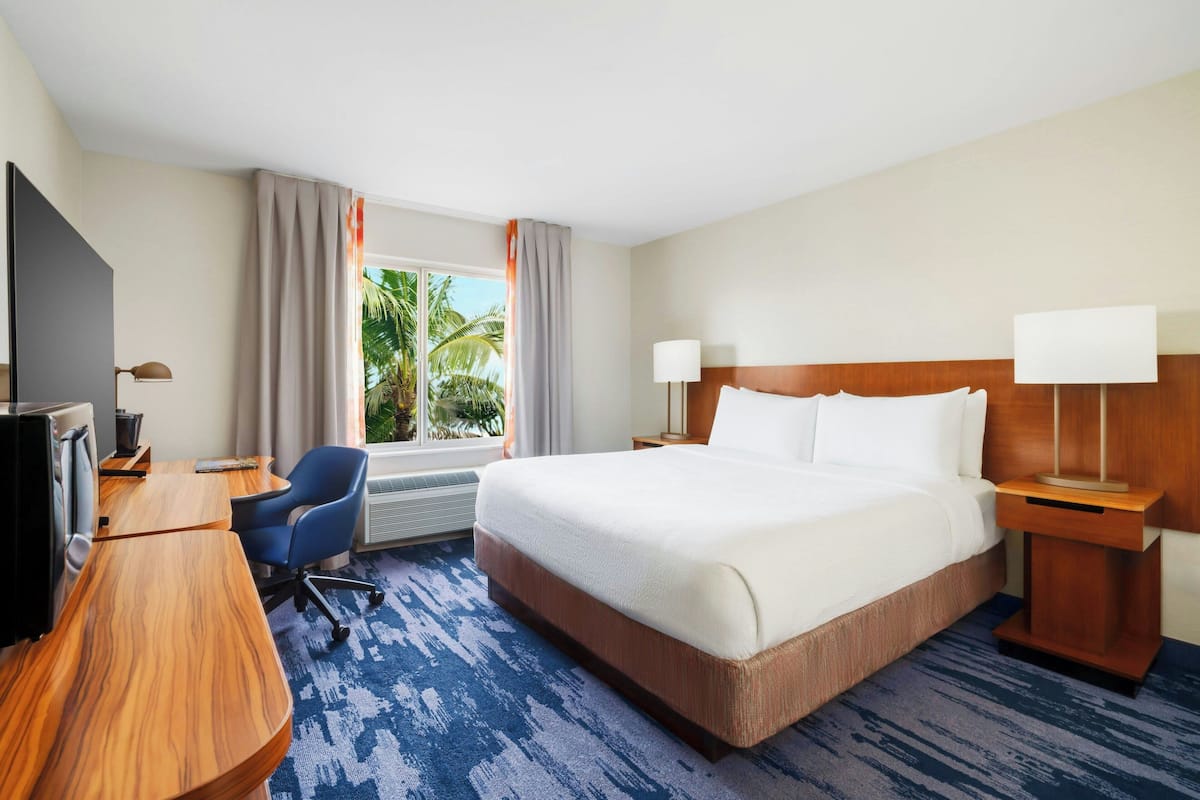 A hotel room with a large bed, a desk with a chair, a television, and a window with curtains.