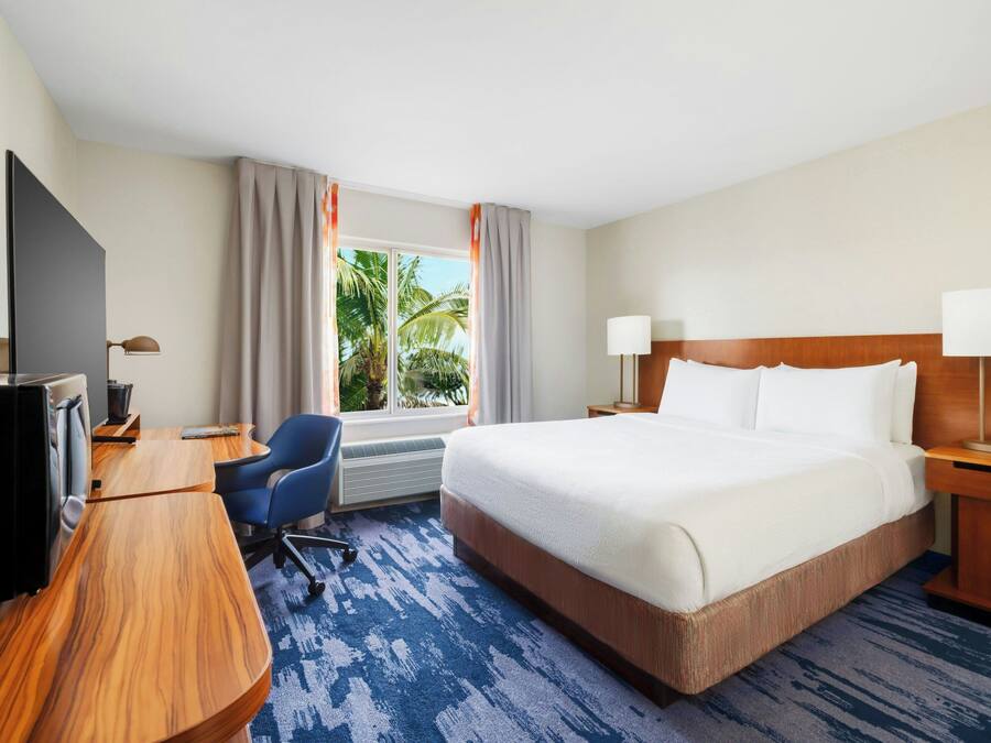 A hotel room with a large bed, a desk with a chair, a television, and a window with curtains.