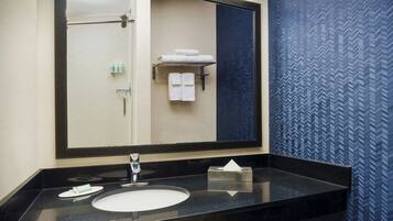 A bathroom with a large mirror, a black countertop, a white sink, and a towel rack with towels.