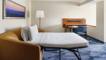 Quarto de hotel com cama, escrivaninha, cadeira, abajur e um quadro na parede.
