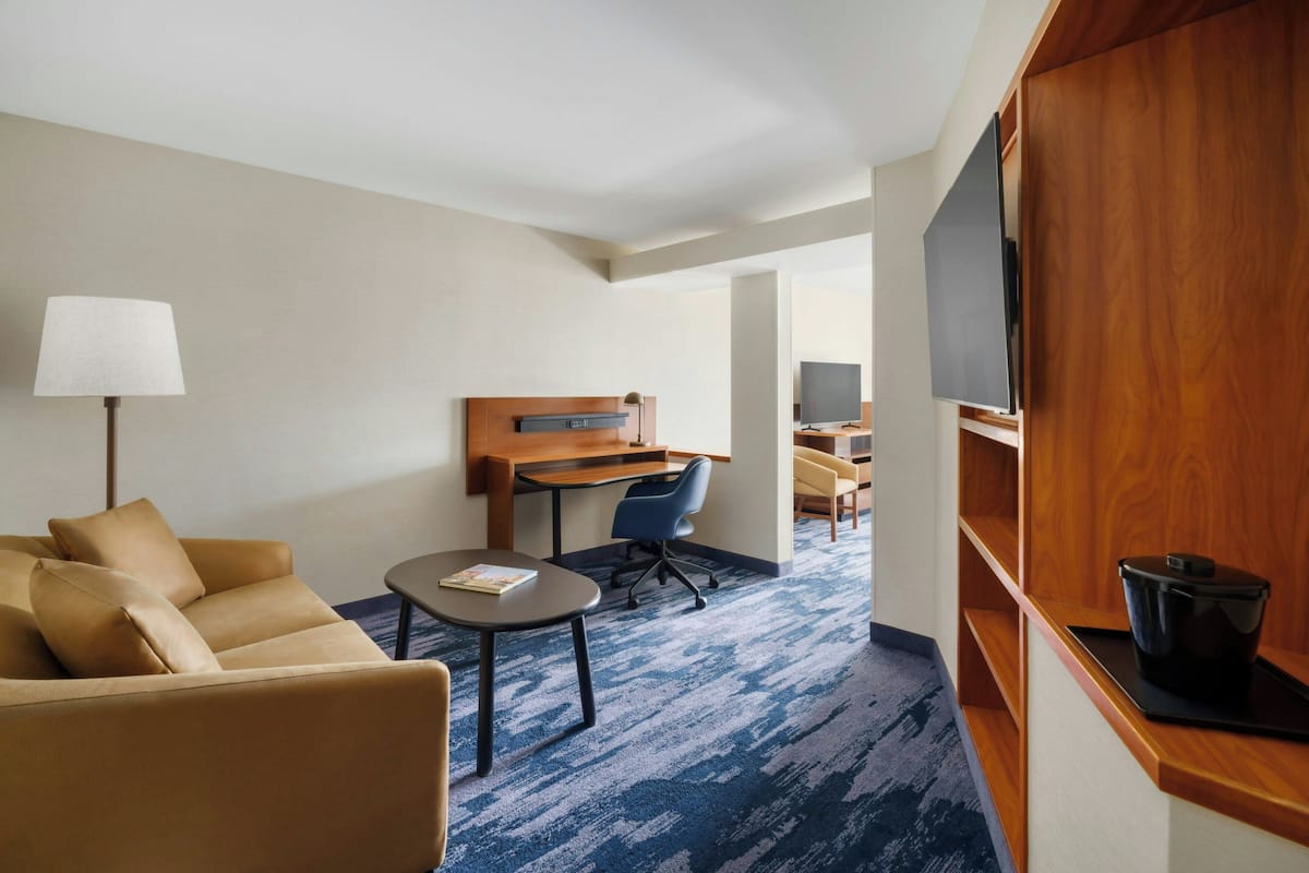 A hotel room with a sofa, a desk, a chair, a lamp, and a television.