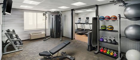 A gym with a bench, dumbbells, treadmills, and various exercise balls.