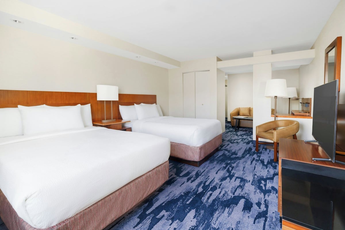 A hotel room with two beds, a TV, a desk, and a chair.