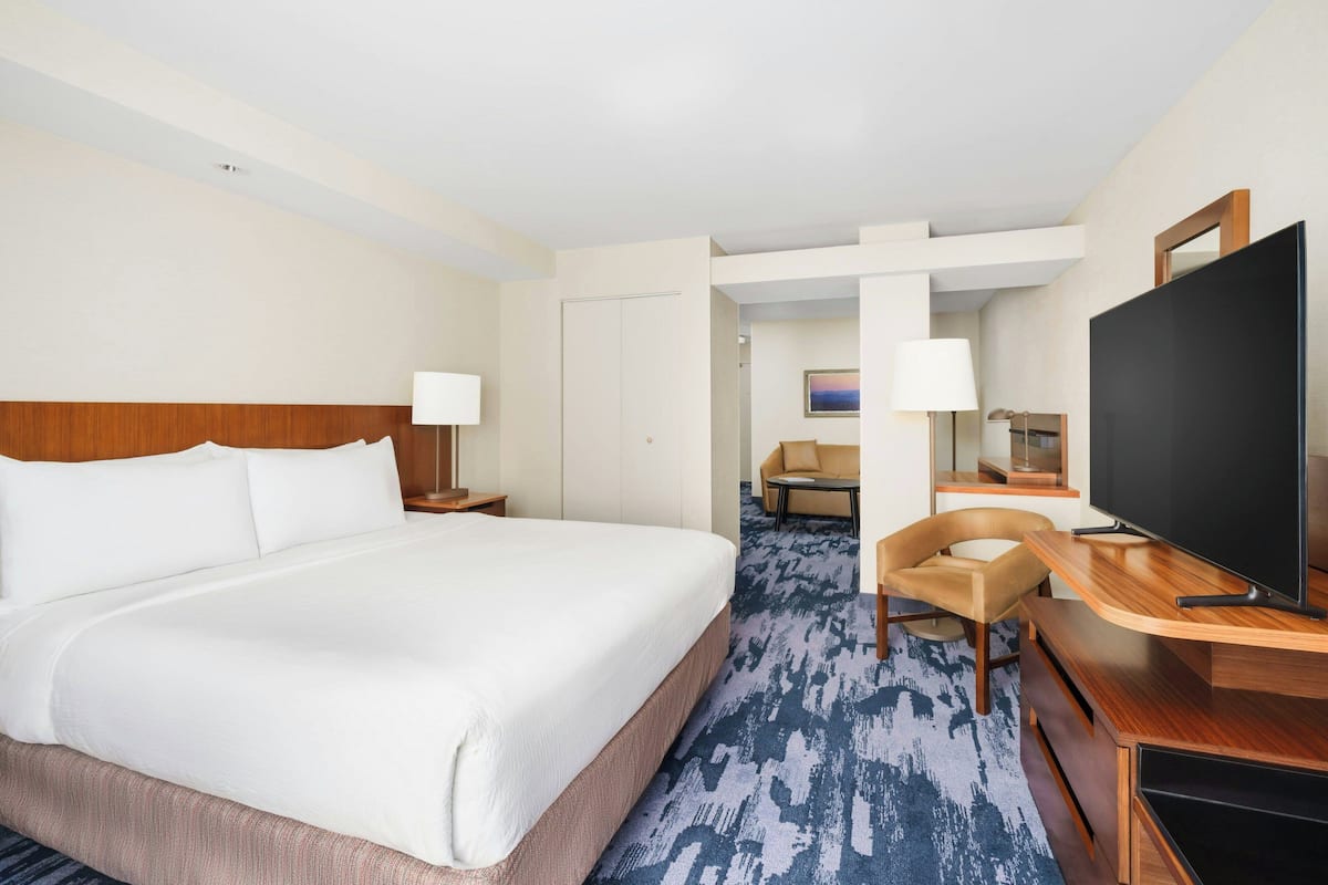 A hotel room with a large bed, a TV, a desk, and a chair.