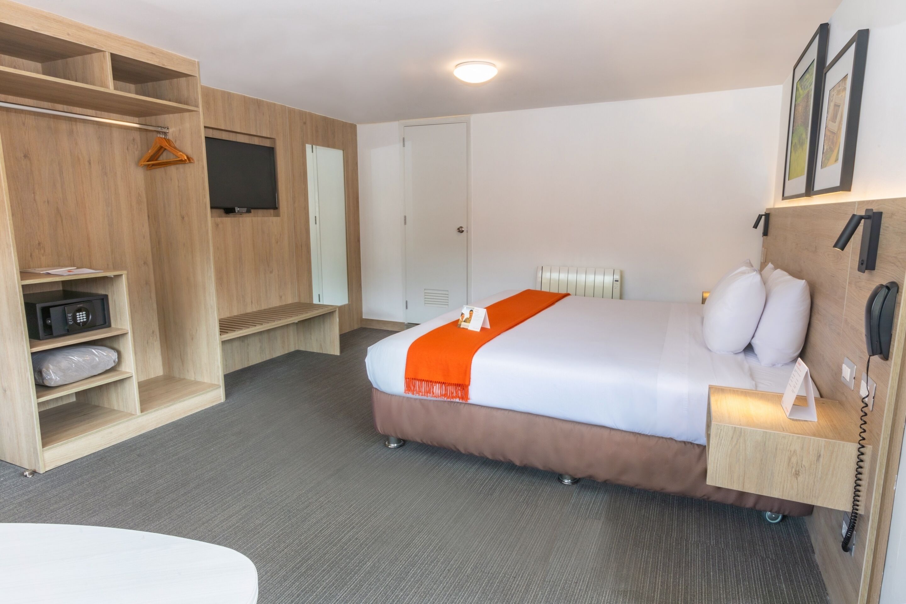 A hotel room with a bed, a wardrobe, a desk, a telephone, and a television.