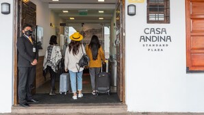 La entrada a Casa Andina Standard Plaza, con una puerta de madera, un cartel y una puerta de vidrio que da al interior.