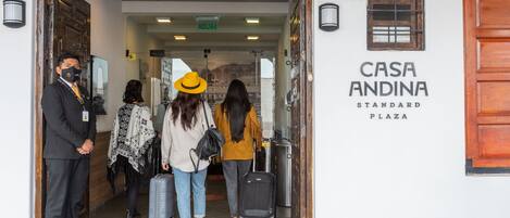 The entrance to Casa Andina Standard Plaza with a wooden door, a signboard, and a glass door leading inside.