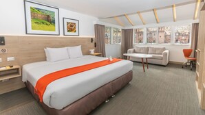 Una habitación de hotel con una cama grande, un sofá, una mesita y amplias ventanas con vistas a la ciudad.