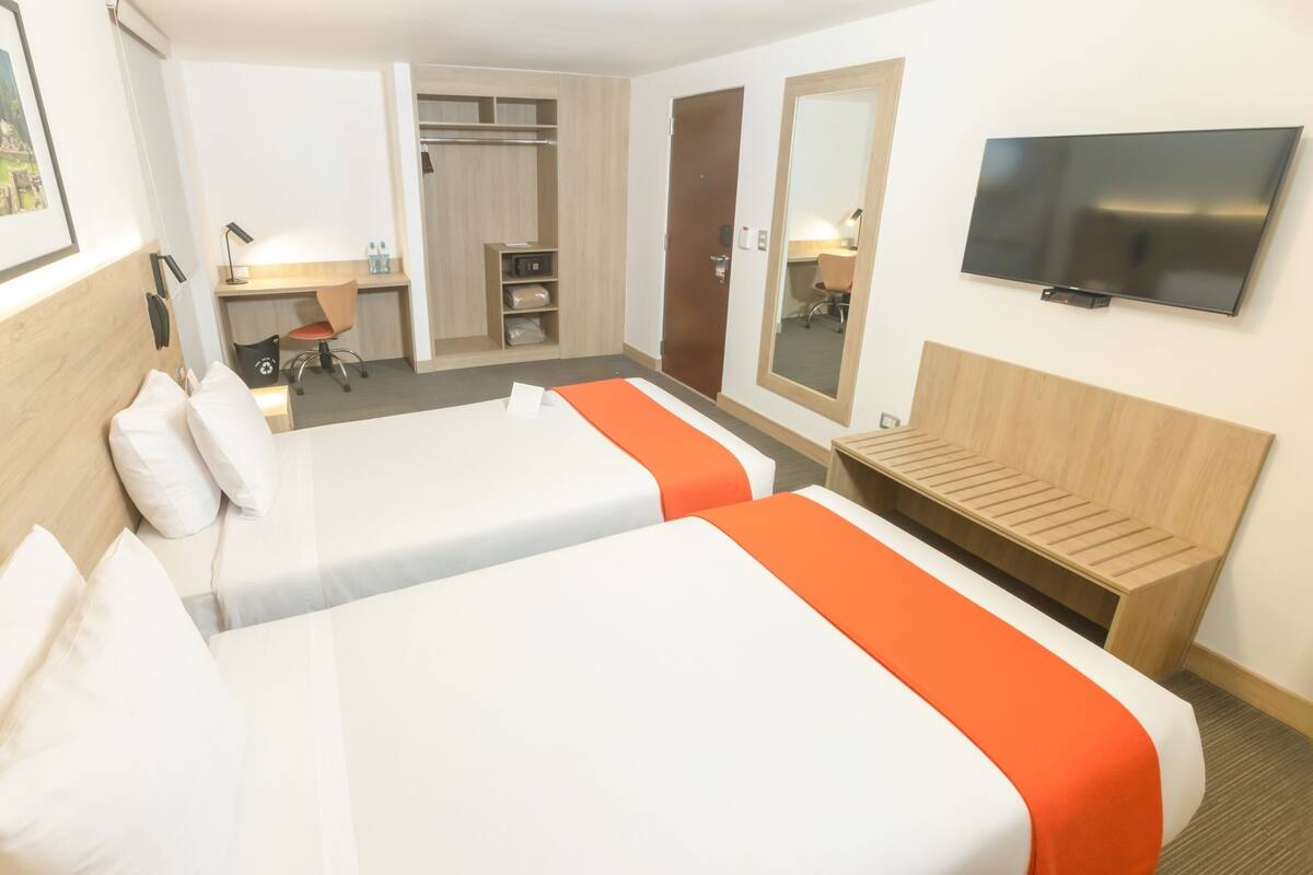 Habitación de hotel con dos camas, un escritorio, una silla, un televisor y un armario.