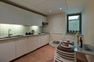 Et køkken med hvide skabe, et flisebeklædt bagpanel og en spiseplads med et bord dækket til to personer.