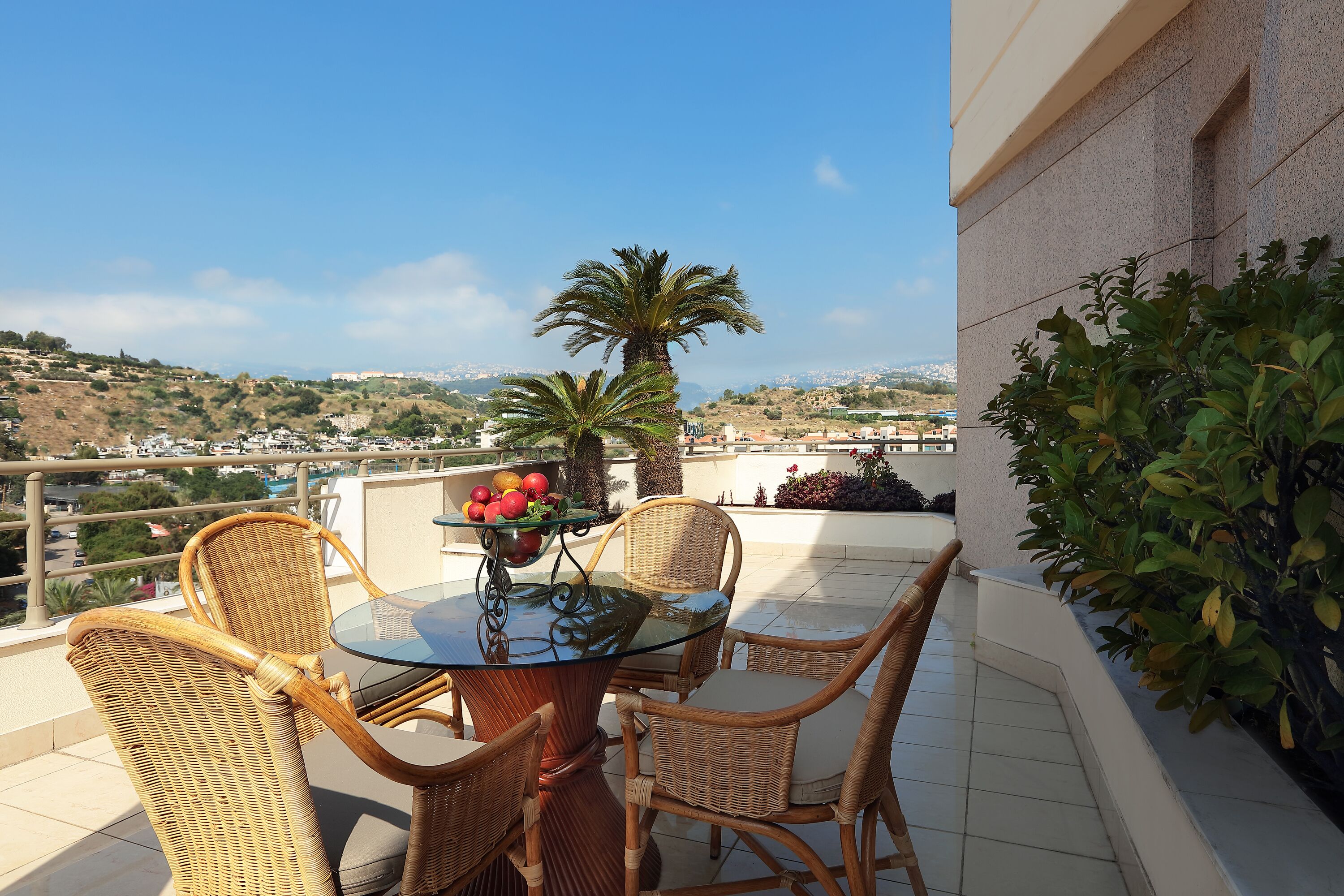A balcony with wicker chairs, a glass table, and a fruit bowl.