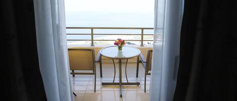 Un balcón con mesa y sillas, un florero con flores y vista al mar.