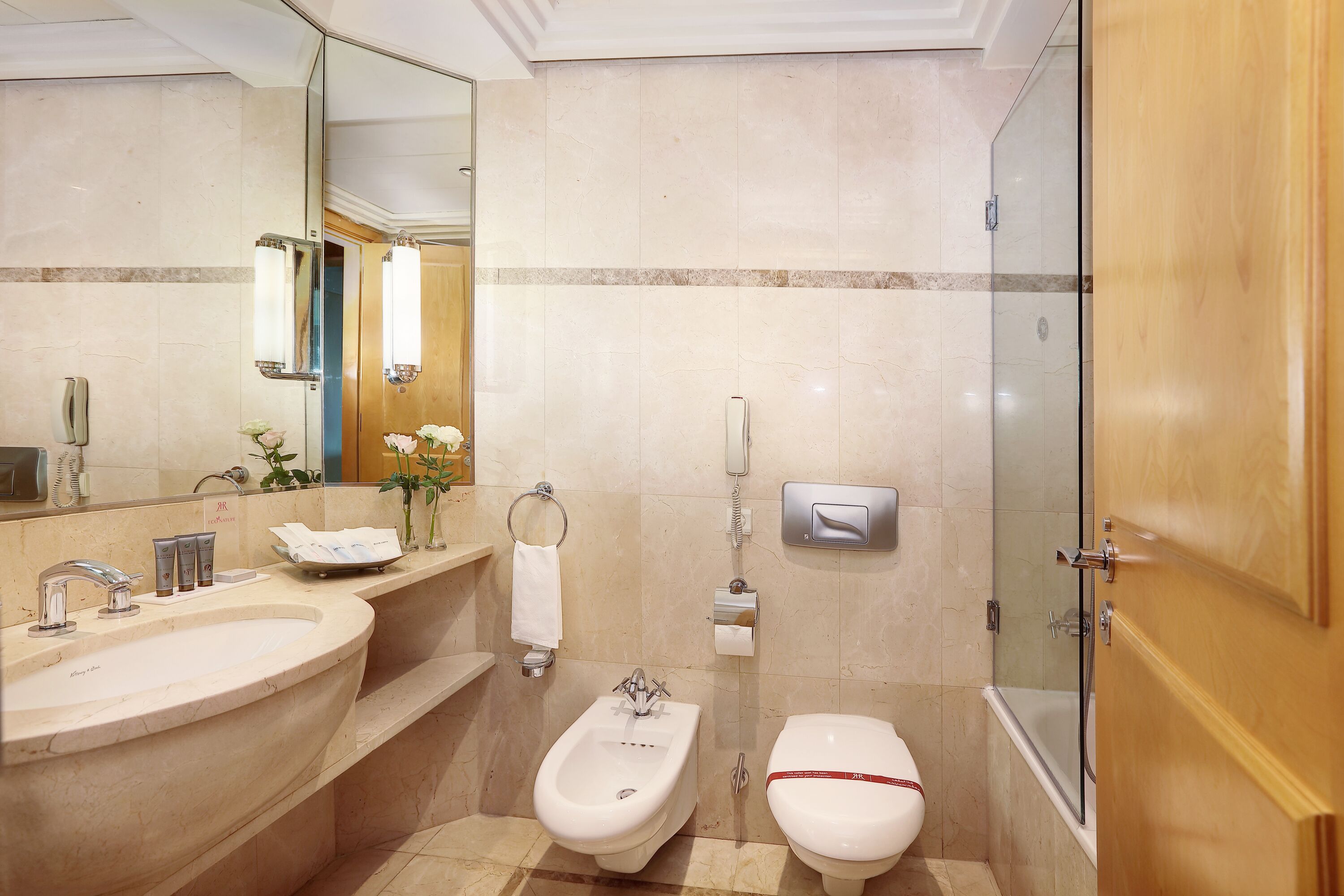 A modern bathroom with a large bathtub, a bidet, a toilet, and a vanity with a sink and mirror.