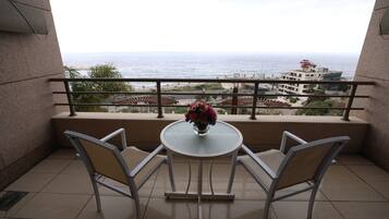 A balcony with a table and chairs, a vase with flowers, and a view of the sea and buildings.