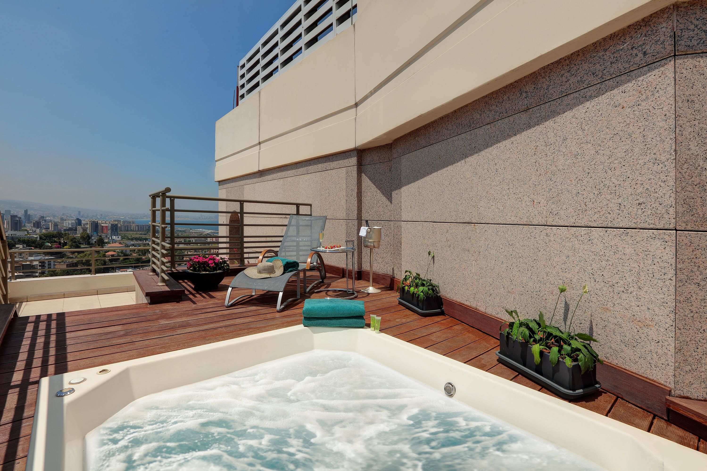 A rooftop terrace with a hot tub, lounge chairs, and potted plants.