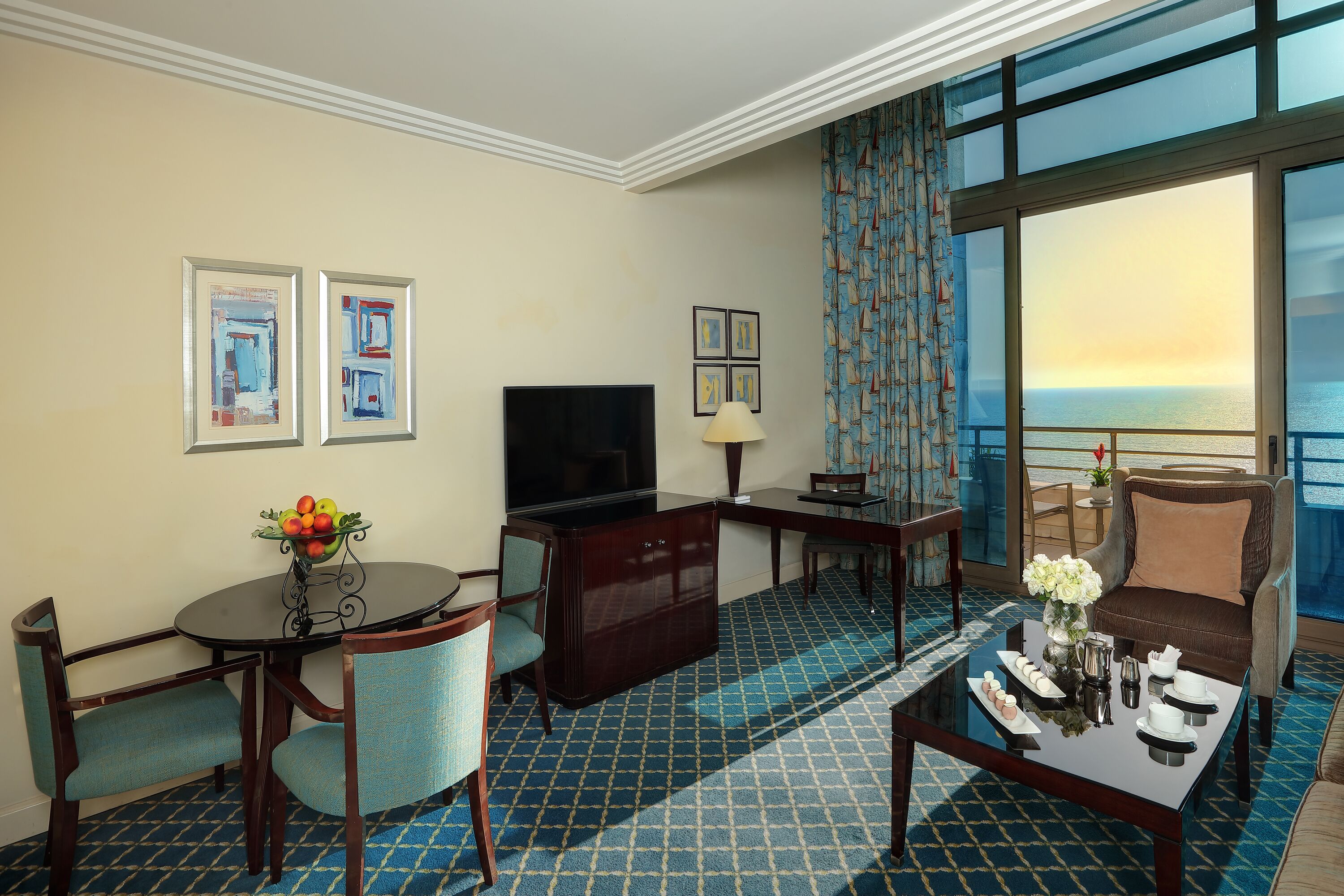 A hotel room with a large window, a flat-screen TV, a dining table with chairs, a sofa, and a decorative vase.