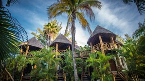 Un complejo turístico con bungalows de techo de paja rodeados de exuberantes palmeras y un cielo despejado.