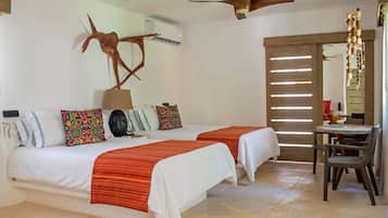Een hotelkamer met twee bedden, een plafondventilator, een zithoek met tafel en stoelen, en een decoratief wandobject.