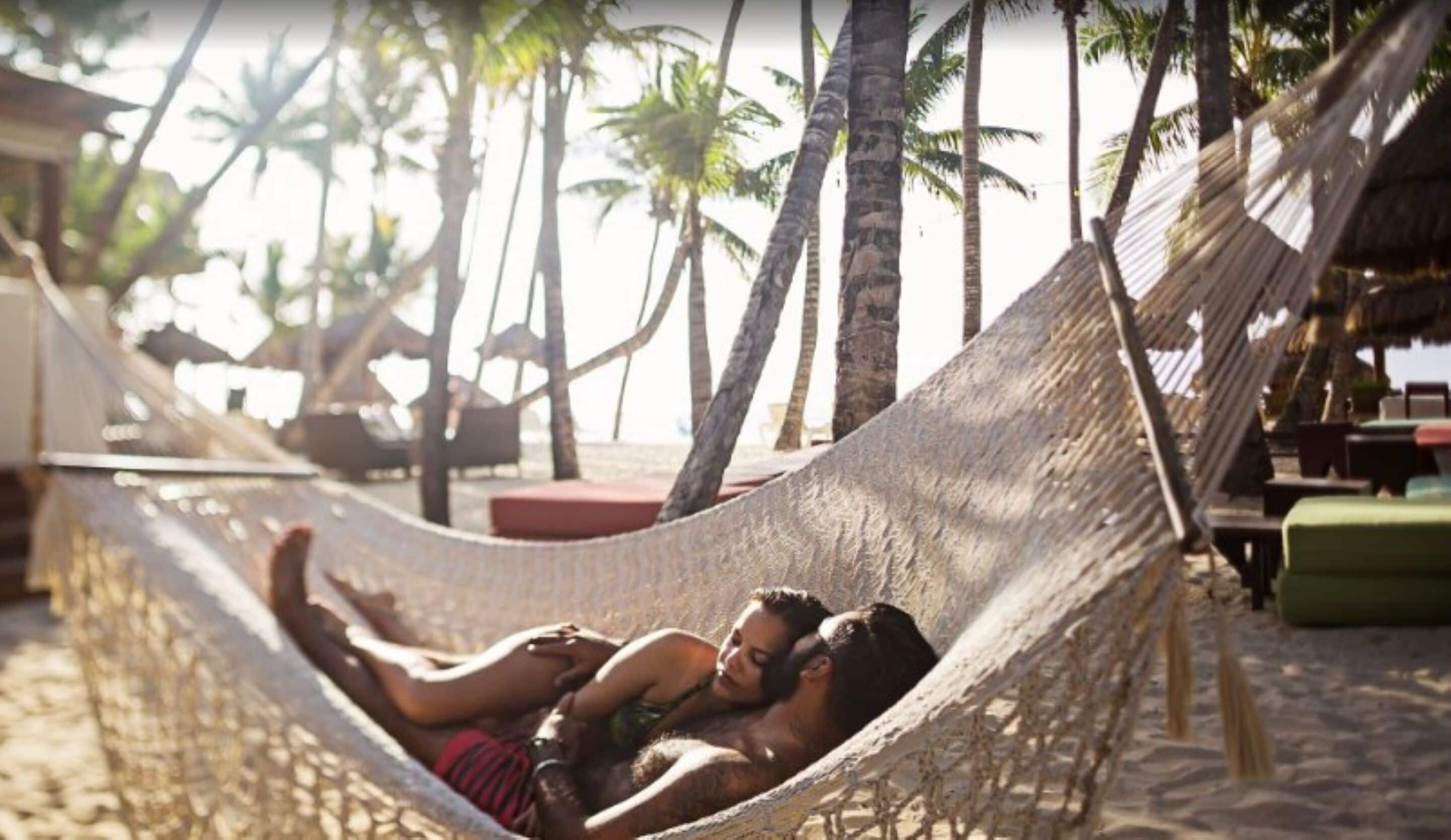 A hammock on a sandy beach with palm trees in the background.
