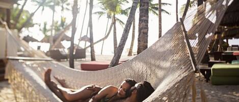 A hammock on a sandy beach with palm trees in the background.