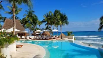 A resort pool with palm trees and a beach view.