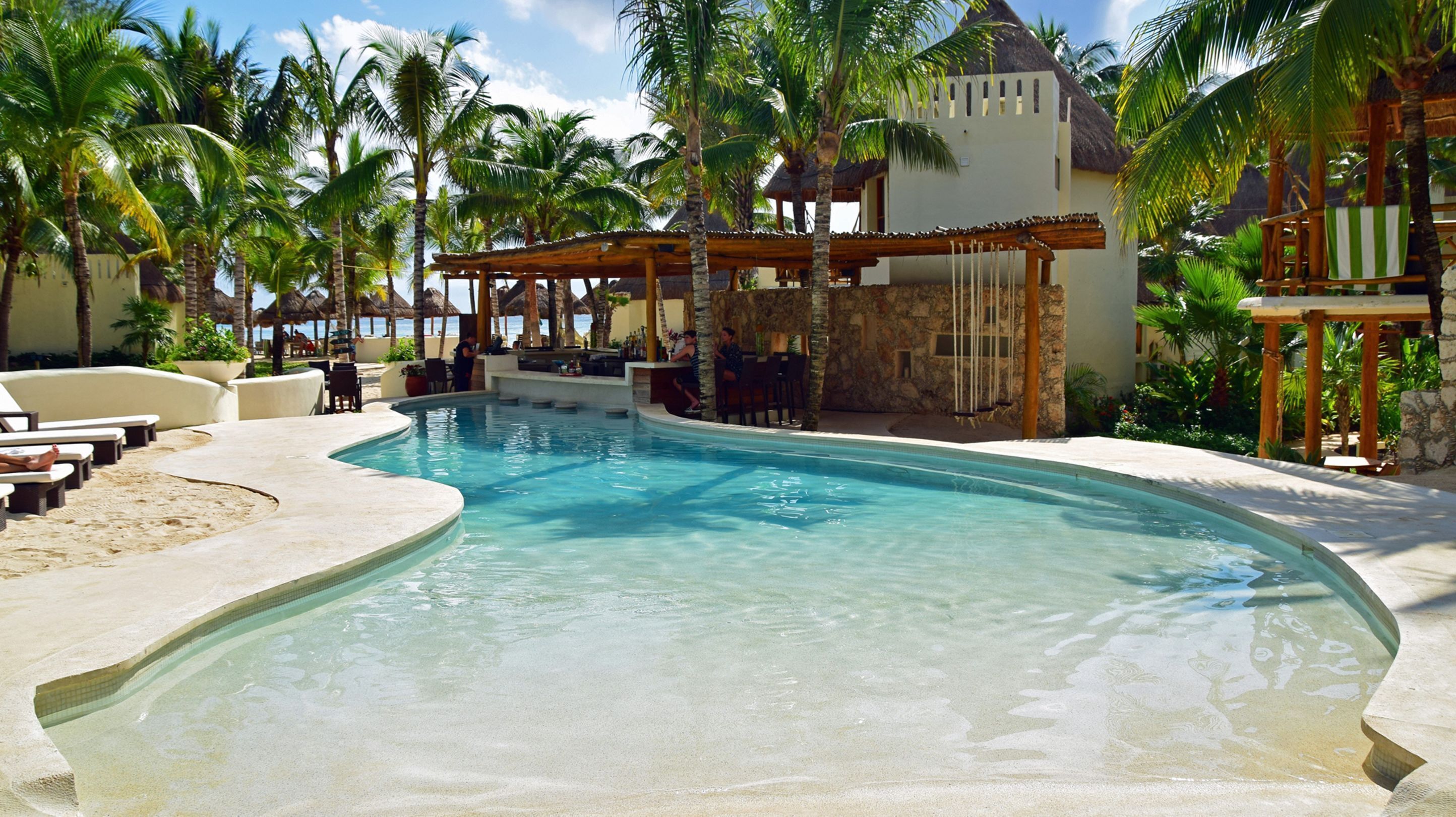 A pool area with lounge chairs, a bar, and palm trees.