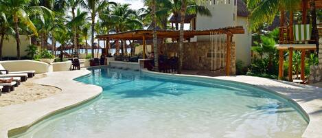 A pool area with lounge chairs, a bar, and palm trees.