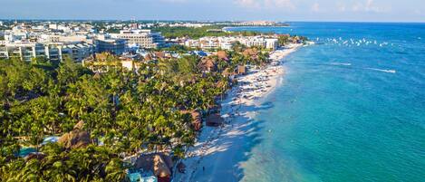 Un complejo turístico costero con alojamiento frente a la playa, palmeras y aguas azul turquesa.