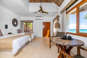 Habitación de hotel con cama, mesa de comedor, ventilador de techo y vista al océano.
