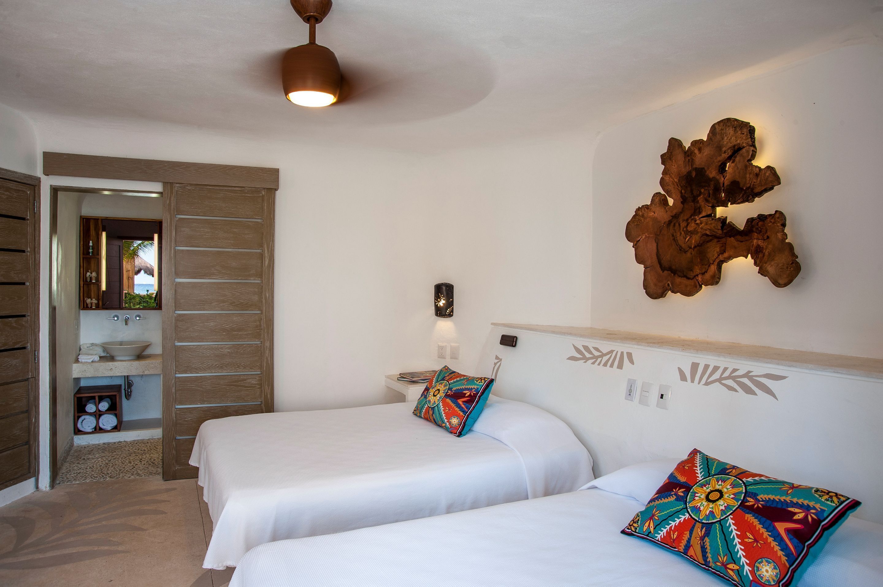 Habitación de hotel con dos camas, un armario de madera, un baño con lavamanos y un adorno en la pared.