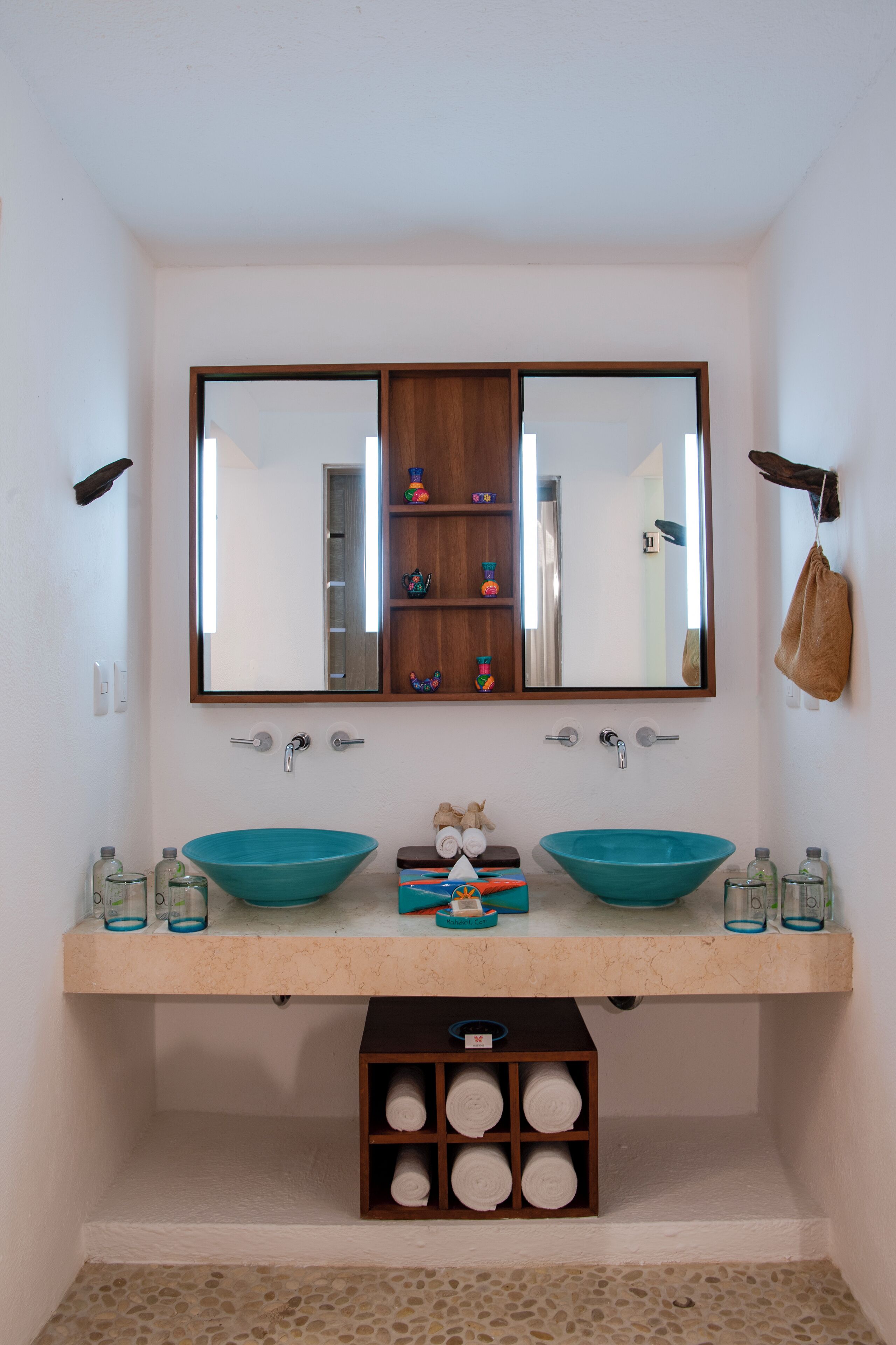 A bathroom with two sinks, a mirror, and a shelf with toiletries.