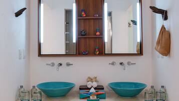 A bathroom with two sinks, a mirror, and a shelf with toiletries.