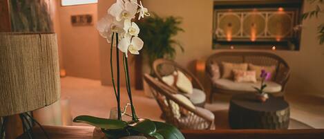 A room with a lamp, a wicker chair, a small table, and a potted orchid.