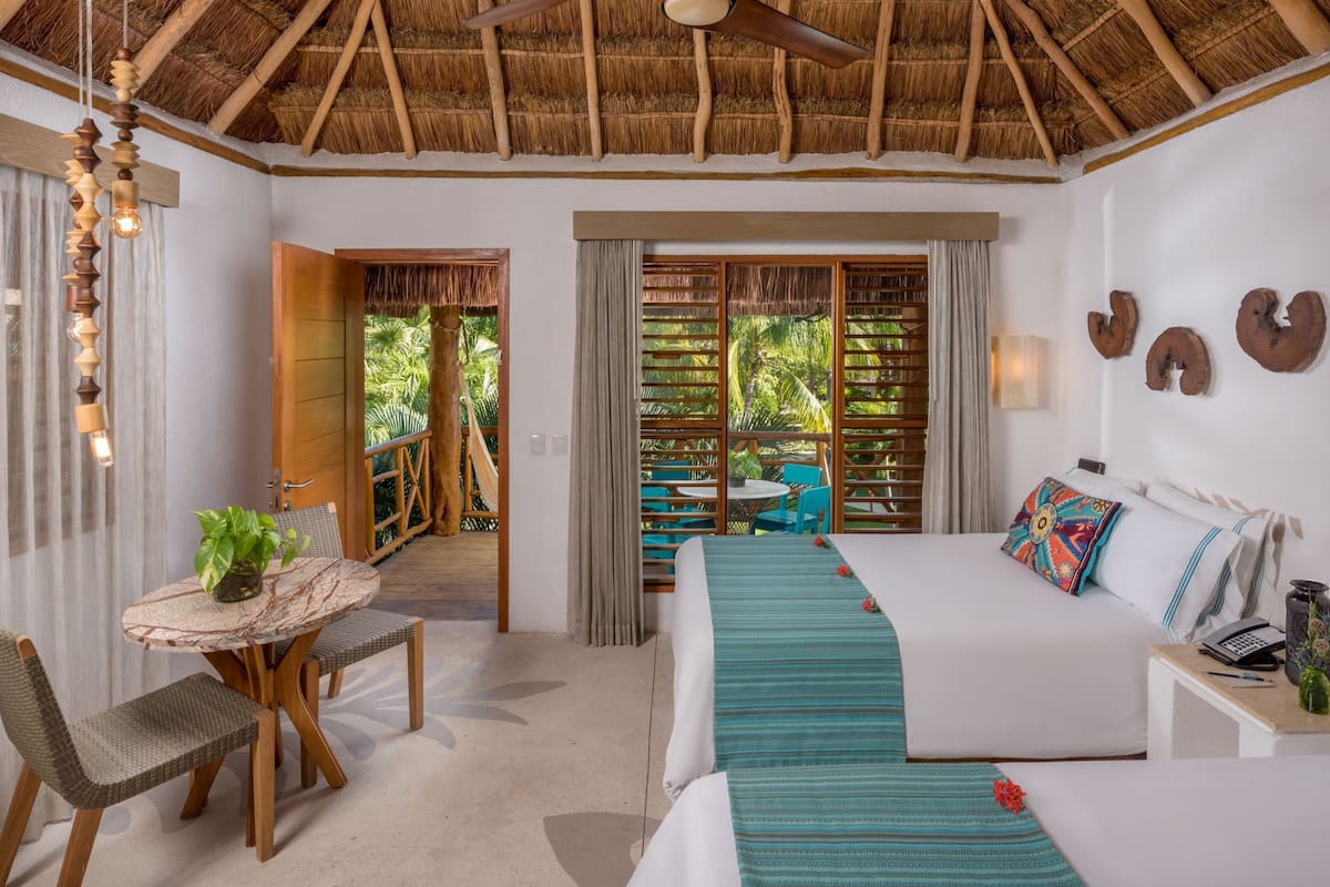A room with a bed, a table with chairs, a ceiling fan, and a view of the outdoors.